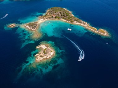 Yunanistan 'ın Sithonia Yarımadası' nda kristal berrak sularla çevrili plajları ve kayaları olan bir adanın havadan görünüşü. Yatlar ve tekneler turkuaz sularda demirliyor. Yakındaki adalar ve resifler görülebilir..