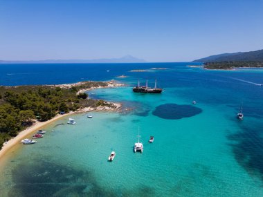 Turkuaz suları, kumlu plajları ve Yunanistan 'ın Sithonia kentinde küçük bir adaya demir atmış bir yelkenli gemisinin bulunduğu kıyı manzarası bir yaz kaçamağının güzelliğini ve macerasını yakalıyor..
