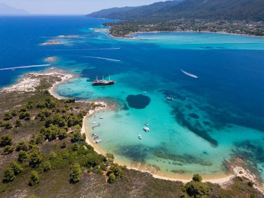 Turkuaz suları, kumlu plajları ve Yunanistan 'ın Sithonia kentinde küçük bir adaya demir atmış bir yelkenli gemisinin bulunduğu kıyı manzarası bir yaz kaçamağının güzelliğini ve macerasını yakalıyor..