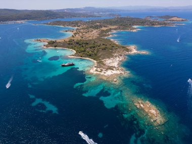 Yunanistan 'ın Sithonia Yarımadası' nda kristal berrak sularla çevrili plajları ve kayaları olan bir adanın havadan görünüşü. Yatlar ve tekneler turkuaz sularda demirliyor. Yakındaki adalar ve resifler görülebilir..