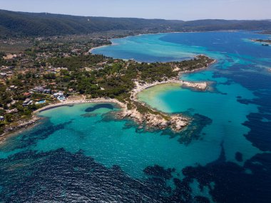Yunanistan 'ın Sithonia Yarımadası' nda kristal berrak sularla çevrili plajları ve kayaları olan bir adanın havadan görünüşü. Yatlar ve tekneler turkuaz sularda demirliyor. Yakındaki adalar ve resifler görülebilir..