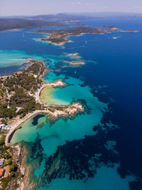 Yunanistan 'ın Sithonia Yarımadası' nda kristal berrak sularla çevrili plajları ve kayaları olan bir adanın havadan görünüşü. Yatlar ve tekneler turkuaz sularda demirliyor. Yakındaki adalar ve resifler görülebilir..