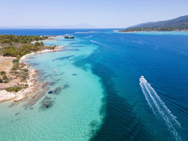 Yunanistan 'ın Sithonia Yarımadası' nda kristal berrak sularla çevrili plajları ve kayaları olan bir adanın havadan görünüşü. Yatlar ve tekneler turkuaz sularda demirliyor. Yakındaki adalar ve resifler görülebilir..