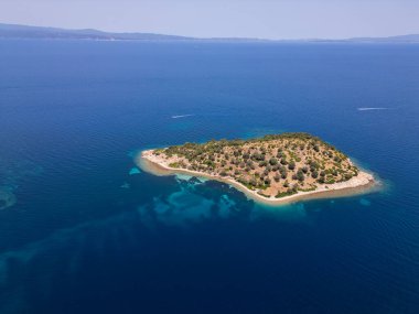 Yunanistan 'ın Sithonia Yarımadası' nda kristal berrak sularla çevrili plajları ve kayaları olan bir adanın havadan görünüşü. Yatlar ve tekneler turkuaz sularda demirliyor. Yakındaki adalar ve resifler görülebilir..