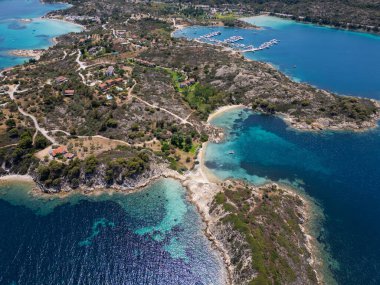 Yunanistan 'ın Sithonia Yarımadası' nda kristal berrak sularla çevrili plajları ve kayaları olan bir adanın havadan görünüşü. Yatlar ve tekneler turkuaz sularda demirliyor. Yakındaki adalar ve resifler görülebilir..