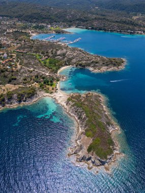 Yunanistan 'ın Sithonia Yarımadası' nda kristal berrak sularla çevrili plajları ve kayaları olan bir adanın havadan görünüşü. Yatlar ve tekneler turkuaz sularda demirliyor. Yakındaki adalar ve resifler görülebilir..