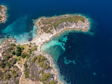 Yunanistan 'ın Sithonia Yarımadası' nda kristal berrak sularla çevrili plajları ve kayaları olan bir adanın havadan görünüşü. Yatlar ve tekneler turkuaz sularda demirliyor. Yakındaki adalar ve resifler görülebilir..