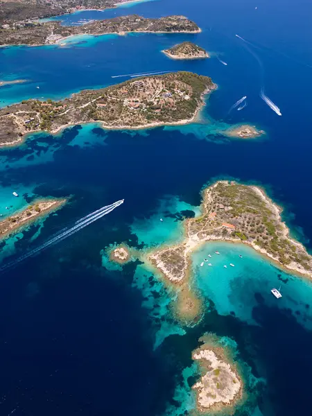 stock image Aerial view of an island on Sithonia Peninsula, Greece, with beaches and rocks, surrounded by crystal-clear waters. Yachts and boats anchor in turquoise waters. Nearby islets and reefs visible.