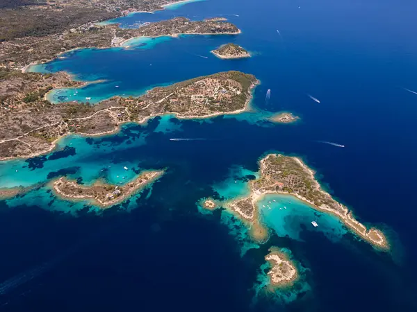 stock image Aerial view of an island on Sithonia Peninsula, Greece, with beaches and rocks, surrounded by crystal-clear waters. Yachts and boats anchor in turquoise waters. Nearby islets and reefs visible.