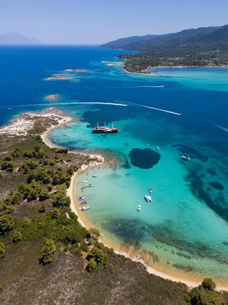 stock image Aerial view of a coastal landscape with turquoise waters, sandy beaches, and a sailing ship anchored near a small island in Sithonia, Greece, capturing the beauty and adventure of a summer getaway.