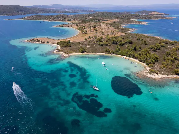 Yunanistan 'ın Sithonia Yarımadası' nda kristal berrak sularla çevrili plajları ve kayaları olan bir adanın havadan görünüşü. Yatlar ve tekneler turkuaz sularda demirliyor. Yakındaki adalar ve resifler görülebilir..
