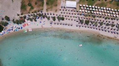 Yunanistan 'ın Sithonia kentindeki renkli şemsiyeler, güneşlikler ve açık turkuaz suların tadını çıkaran plaj sakinlerinin canlı yaz atmosferini yakaladığı canlı bir sahil manzarası..