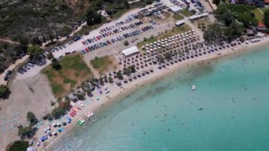 Yunanistan 'ın Sithonia kentindeki renkli şemsiyeler, güneşlikler ve açık turkuaz suların tadını çıkaran plaj sakinlerinin canlı yaz atmosferini yakaladığı canlı bir sahil manzarası..