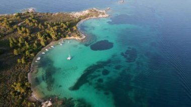 Yunanistan 'ın Sithonia Yarımadası' nda kristal berrak sularla çevrili plajları ve kayaları olan bir adanın havadan görünüşü. Yatlar ve tekneler turkuaz sularda demirliyor. Yakındaki adalar ve resifler görülebilir..