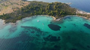 Yunanistan 'ın Sithonia Yarımadası' nda kristal berrak sularla çevrili plajları ve kayaları olan bir adanın havadan görünüşü. Yatlar ve tekneler turkuaz sularda demirliyor. Yakındaki adalar ve resifler görülebilir..