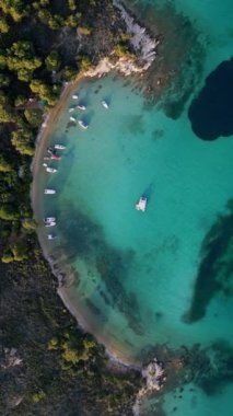 Yunanistan 'ın Sithonia Yarımadası' nda kristal berrak sularla çevrili plajları ve kayaları olan bir adanın havadan görünüşü. Yatlar ve tekneler turkuaz sularda demirliyor. Yakındaki adalar ve resifler görülebilir..