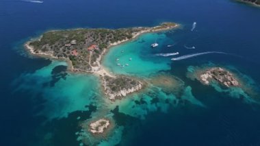 Yunanistan 'ın Sithonia Yarımadası' nda kristal berrak sularla çevrili plajları ve kayaları olan bir adanın havadan görünüşü. Yatlar ve tekneler turkuaz sularda demirliyor. Yakındaki adalar ve resifler görülebilir..