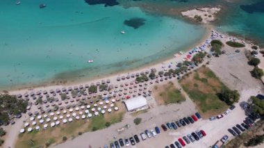 Yunanistan 'ın Sithonia kentindeki renkli şemsiyeler, güneşlikler ve açık turkuaz suların tadını çıkaran plaj sakinlerinin canlı yaz atmosferini yakaladığı canlı bir sahil manzarası..