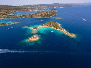 Yunanistan 'ın Sithonia Yarımadası' nda kristal berrak sularla çevrili plajları ve kayaları olan bir adanın havadan görünüşü. Yatlar ve tekneler turkuaz sularda demirliyor. Yakındaki adalar ve resifler görülebilir..