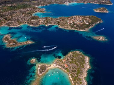 Yunanistan 'ın Sithonia Yarımadası' nda kristal berrak sularla çevrili plajları ve kayaları olan bir adanın havadan görünüşü. Yatlar ve tekneler turkuaz sularda demirliyor. Yakındaki adalar ve resifler görülebilir..