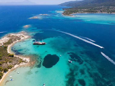 Turkuaz suları, kumlu plajları ve Yunanistan 'ın Sithonia kentinde küçük bir adaya demir atmış bir yelkenli gemisinin bulunduğu kıyı manzarası bir yaz kaçamağının güzelliğini ve macerasını yakalıyor..
