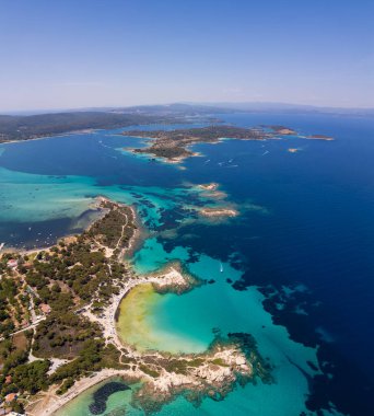 Yunanistan 'ın Sithonia Yarımadası' nda kristal berrak sularla çevrili plajları ve kayaları olan bir adanın havadan görünüşü. Yatlar ve tekneler turkuaz sularda demirliyor. Yakındaki adalar ve resifler görülebilir..