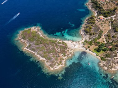 Yunanistan 'ın Sithonia Yarımadası' nda kristal berrak sularla çevrili plajları ve kayaları olan bir adanın havadan görünüşü. Yatlar ve tekneler turkuaz sularda demirliyor. Yakındaki adalar ve resifler görülebilir..