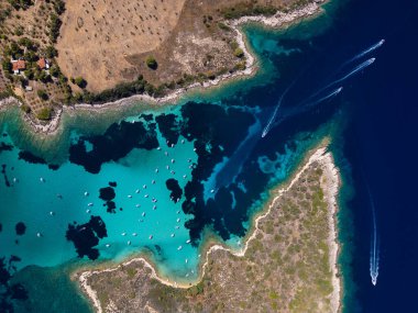 Berrak sularda yüzen, mercan resiflerinin karanlık kısımlarıyla çevrili turkuaz bir lagünün havadan görünüşü canlı ve sakin deniz manzarasını gözler önüne seriyor..