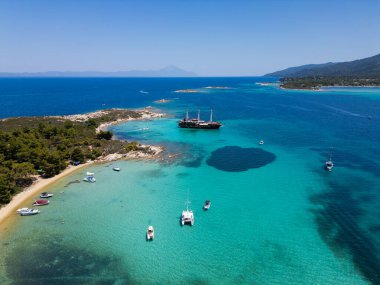 Turkuaz suları, kumlu plajları ve Yunanistan 'ın Sithonia kentinde küçük bir adaya demir atmış bir yelkenli gemisinin bulunduğu kıyı manzarası bir yaz kaçamağının güzelliğini ve macerasını yakalıyor..