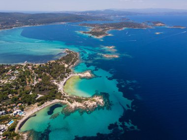 Yunanistan 'ın Sithonia Yarımadası' nda kristal berrak sularla çevrili plajları ve kayaları olan bir adanın havadan görünüşü. Yatlar ve tekneler turkuaz sularda demirliyor. Yakındaki adalar ve resifler görülebilir..