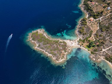 Yunanistan 'ın Sithonia Yarımadası' nda kristal berrak sularla çevrili plajları ve kayaları olan bir adanın havadan görünüşü. Yatlar ve tekneler turkuaz sularda demirliyor. Yakındaki adalar ve resifler görülebilir..