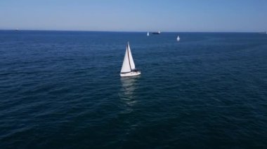 Sakin, mavi sularda, berrak bir gökyüzünün altında süzülen sakin bir yelkenli. Uzak gemiler ve yelkenliler ufukta belirdi. Huzurlu bir deniz manzarası yarattılar..