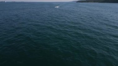 Bir insan açık denizde jet ski ile hızla ilerlerken arkasında dinamik bir beyaz su izi bırakır. Su sporlarının enerjik enerjisi derin mavi okyanus zeminine yansıyor..