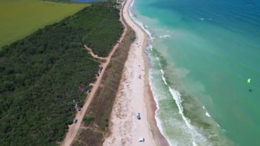 Sahil boyunca dağınık çadırları ve şemsiyeleri olan kumlu bir sahil manzarası. Dalgalar yavaşça kıyıya vurur, okyanus kıyısında huzurlu ve rahatlatıcı bir yaz gününü yakalar..