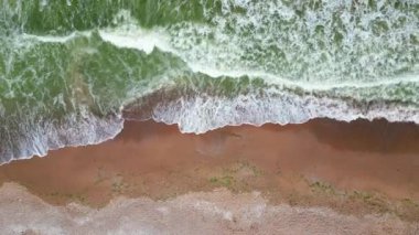 Okyanus dalgalarının kumlu bir sahile çarpması, zümrüt yeşili su ile sıcak, desenli kum arasında güzel bir kontrastlık yaratır. Mükemmel bir sahil güzelliği görüntüsü..