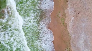 Okyanus dalgalarının kumlu bir sahile çarpması, zümrüt yeşili su ile sıcak, desenli kum arasında güzel bir kontrastlık yaratır. Mükemmel bir sahil güzelliği görüntüsü..