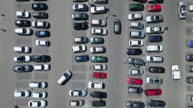 Tepetaklak bir perspektiften çekilen, çeşitli arabalarla dolu bir otoparkın insansız hava aracı videosu. Görüntüler, şehir ortamındaki organize araç sıralarını vurguluyor.