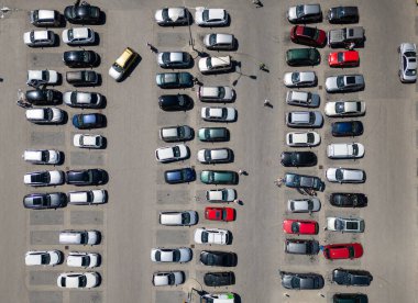 Düzenli arabalarla dolu kalabalık bir otoparkın havadan görüntüsü. Fotoğraf, şehir otoparkının organize yapısını yakalıyor, tepeden tırnağa çeşitli araçları vurguluyor..