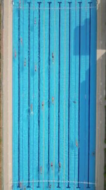 Yüzücülerin açık mavi bir havuzda, yukarıdan çekilen drone videosu. Yukarıdan aşağıya bakış, yüzücülerin ritmik hareketlerini ve suyun canlı, ferahlatıcı atmosferini vurgular..