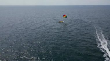 Aşağıdaki bir sürat teknesi tarafından çekilen, açık denizde süzülen renkli bir deniz paraşütünün insansız hava aracı videosu. Uçsuz bucaksız, sakin deniz manzarasına karşı paraşütle atlamanın heyecanını ve özgürlüğünü yakalıyor..