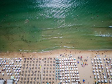 Kalabalık bir plajın, okyanusun nazik dalgalarına karşı dizilmiş şemsiyeli ve güneşli videoları. Hava görüntüsü, bir yaz gününün canlı atmosferini yakalar. Bulgaristan.