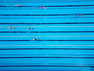 Yüzücülerin açık mavi bir havuzda, yukarıdan çekilen drone videosu. Yukarıdan aşağıya bakış, yüzücülerin ritmik hareketlerini ve suyun canlı, ferahlatıcı atmosferini vurgular..