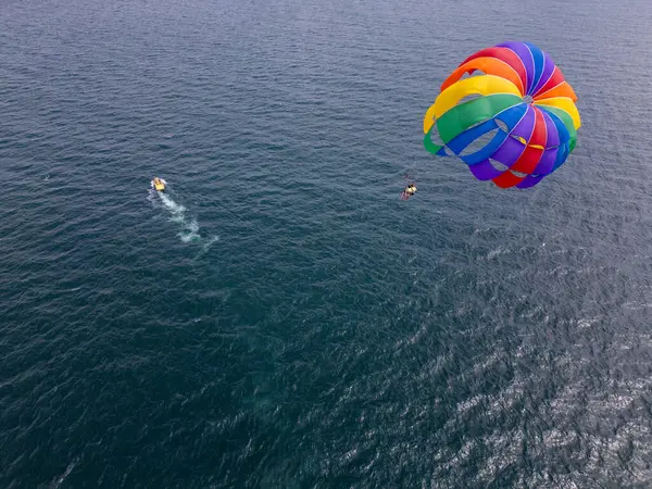 stock image Drone video of a colorful parasail soaring over the open ocean, towed by a speedboat below. The aerial view captures the thrill and freedom of parasailing against a vast, serene seascape.