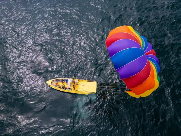 stock image Drone video of a colorful parasail soaring over the open ocean, towed by a speedboat below. The aerial view captures the thrill and freedom of parasailing against a vast, serene seascape.