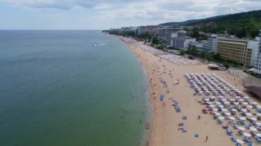 Deniz kenarında güneşli bir günün tadını çıkaran şemsiyelerle dolu güzel bir sahil manzarası. Yaz tatillerini, sahil tatil beldelerini ve seyahat deneyimlerini desteklemek için ideal. Altın kumlar