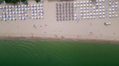 İHA videosu, sahilin tepesinden aşağıya doğru renkli şemsiyelerin sıralandığı sahilin sahil şeridinin yanındaki kumsala mükemmel bir şekilde dizilmiş halini çekiyor. Canlı sahne yaz rahatlığını sergiliyor.