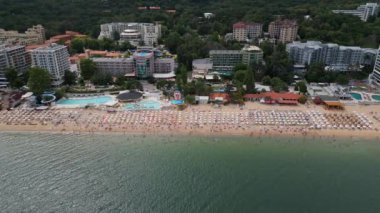 Deniz kenarında güneşli bir günün tadını çıkaran şemsiyelerle dolu güzel bir sahil manzarası. Yaz tatillerini, sahil tatil beldelerini ve seyahat deneyimlerini desteklemek için ideal. Altın kumlar