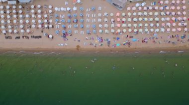 Deniz kenarında güneşli bir günün tadını çıkaran şemsiyelerle dolu güzel bir sahil manzarası. Yaz tatillerini, sahil tatil beldelerini ve seyahat deneyimlerini desteklemek için ideal. Altın kumlar