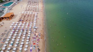 Kalabalık bir plajın renkli şemsiyeli ve denizde yüzen yüzücülerin canlı bir yaz gününün özünü yakaladığı görüntüler. Seyahat, turizm ve plaj yaşam tarzı promosyonu için mükemmel. Altın kumlar