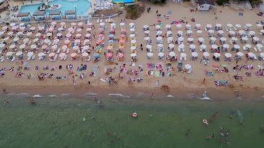 Kalabalık bir plajın renkli şemsiyeli ve denizde yüzen yüzücülerin canlı bir yaz gününün özünü yakaladığı görüntüler. Seyahat, turizm ve plaj yaşam tarzı promosyonu için mükemmel. Altın kumlar